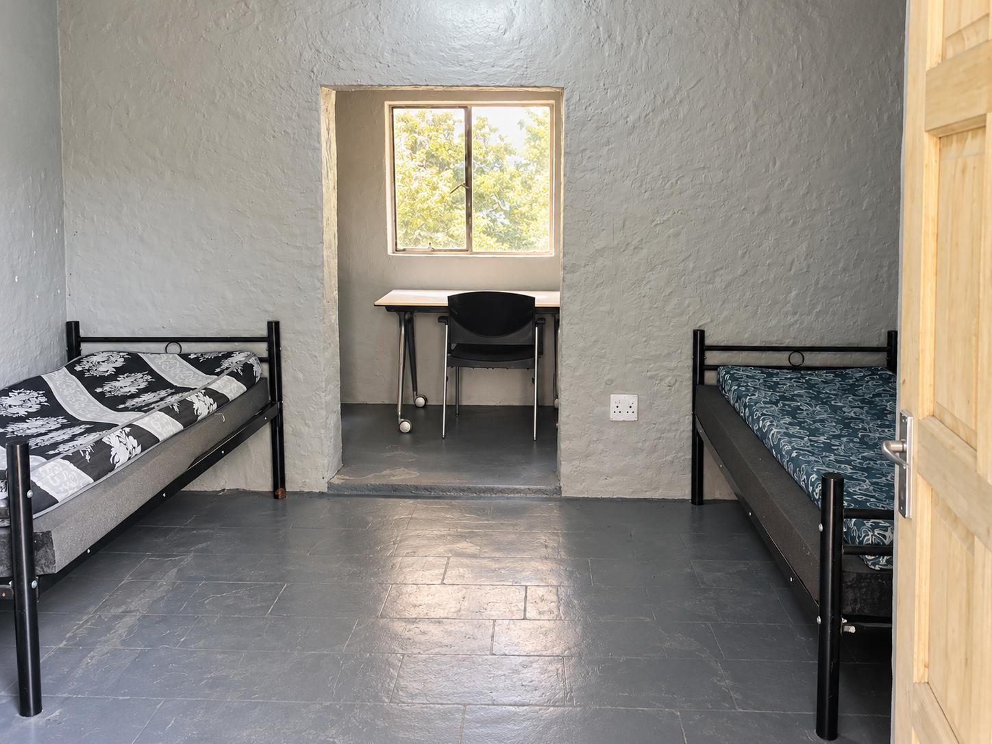 Two single beds in a shared room, with a desk and chair by the window