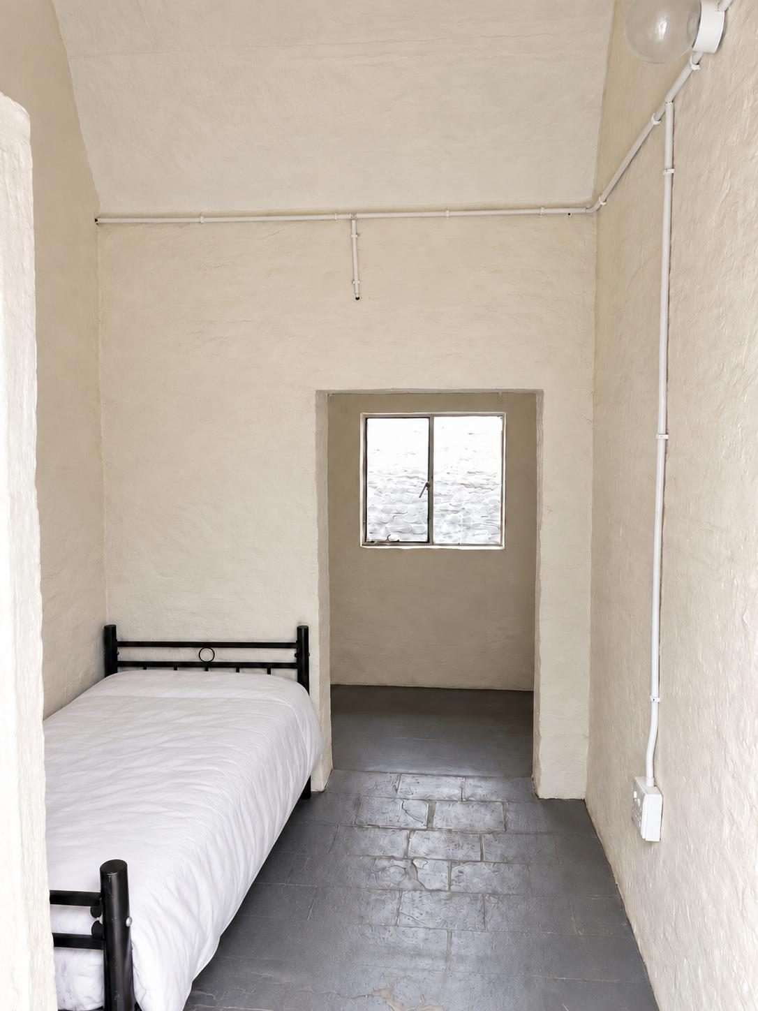 A single bed with white bedding in a narrow cream-walled room