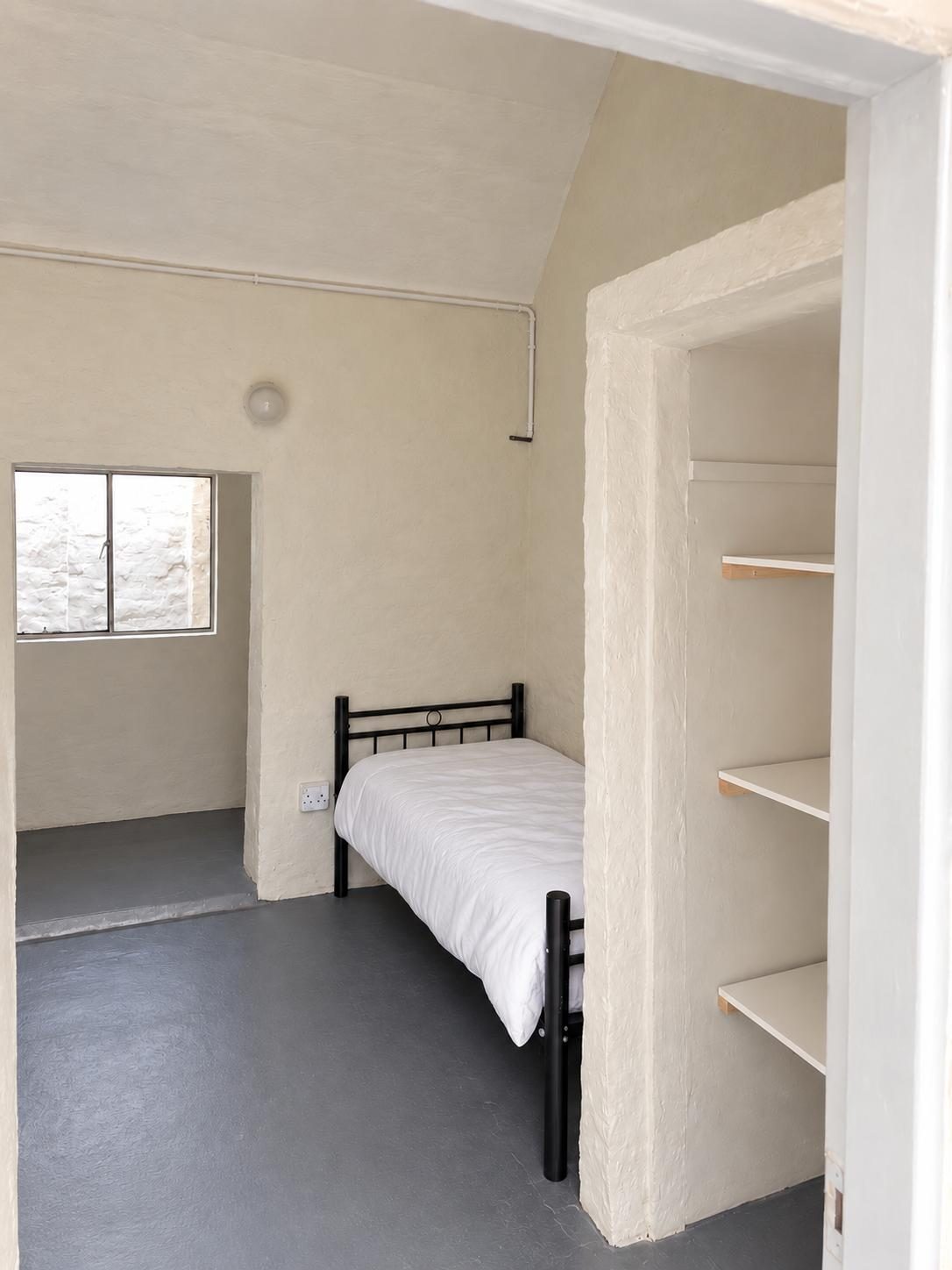 A single bed seen from the doorway, with shelves in the passage